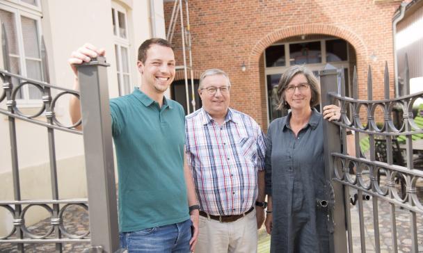 3 Personen vor Eingangspforte eines Hauses