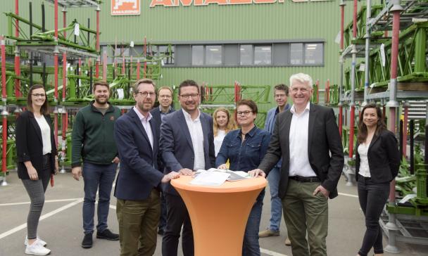 Eine Personengruppe steht vor einem Fabrikgebäude.
