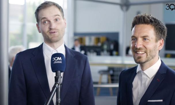 Zwei Personen mit Mikrofon stehen vor einer Kamera.