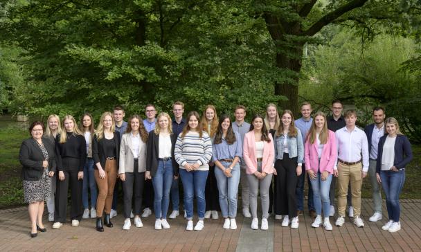 Eine Personengruppe steht vor einem Baum.