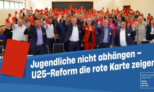 Eine Personengruppe in einem Saal hält rote Karten in die Höhe.