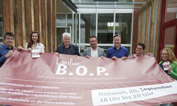 Sieben Personen mit einem Werbebanner in den Händen stehen vor einem Gebäude.