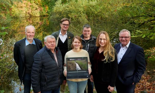 Eine Personengruppe steht vor einem kleinen See