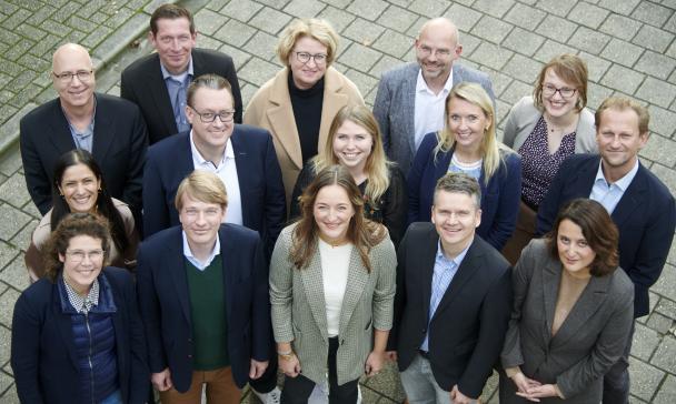 Eine Personengruppe steht vor einem Gebäude und schaut nach oben.