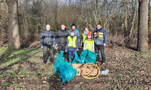 Eine Personengruppe mit Müllsäcken steht am Rande eines Waldes.