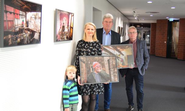 Vier Personen mit Fotos in den Händen stehen in einem Flur mit Fotos an den Wänden.