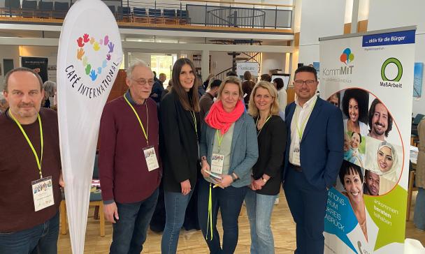 Sechs Personen stehen in einer Halle neben einem Roll-Up-Poster.