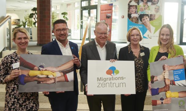 Fünf Personen stehen im Foyer eines Gebäudes vor einer Treppe.