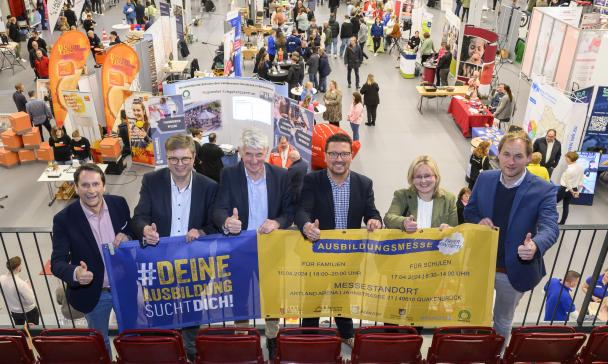 Sechs Personen mit einem Werbebanner in den Händen stehen auf der Empore einer Sporthalle.