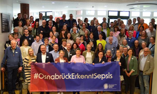 Eine große Personengruppe steht auf einer Treppe in einem Foyer.