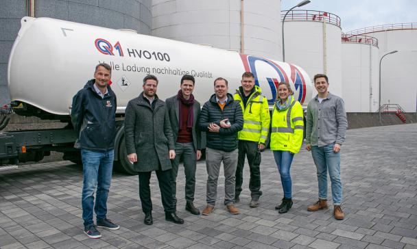 Eine Personengruppe steht vor einem Tanklastzug.