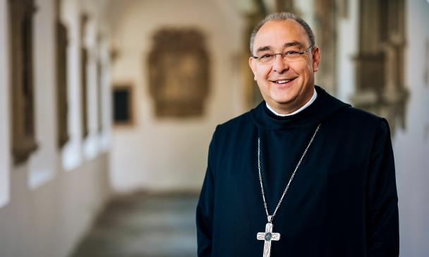 Eine Person in Ordenstracht steht in einem Klostergang.