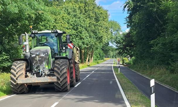 Straße mit Radweg. Auf der Straße fährt ein Traktor.