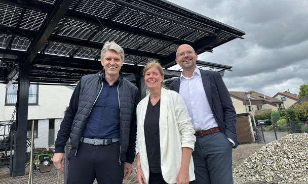 Drei Personen stehen vor einem Solarcarport.