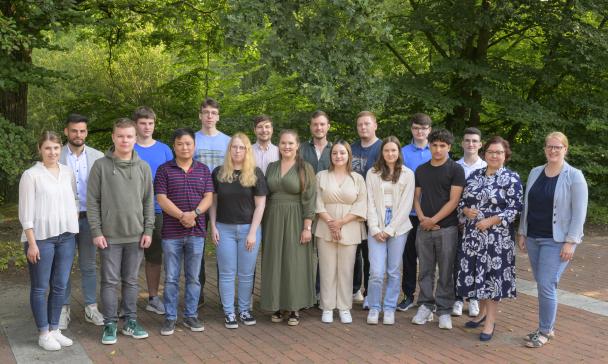 Eine Personengruppe steht vor einem Wäldchen.