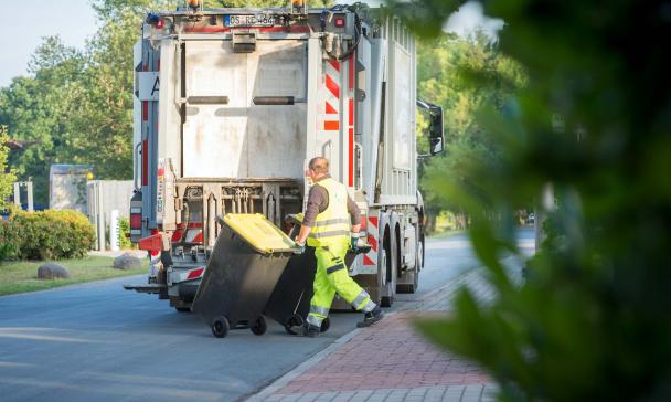 Eine Person rollt eine gelbe Tonne zu einem Abfallfahrzeug.