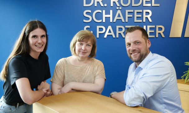 Drei Personen stehen an einem Tisch.