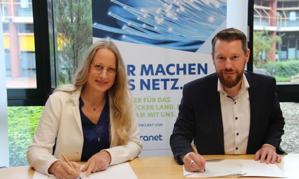 Zwei Personen mit Stiften in den Händen sitzen an einem Tisch, auf dem Papiere liegen.