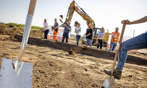 Eine Personengruppe mit Spaten in den Händen steht auf einer Baustelle.