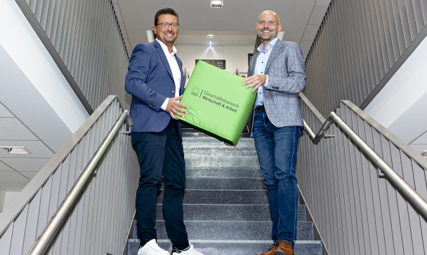 Zwei Personen mit einem großen Würfel in den Händen stehen in einem Treppenhaus.