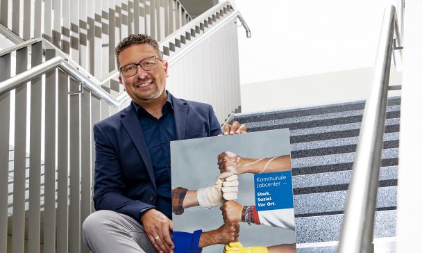 Eine Person mit einem Schild in den Händen sitzt auf einer Treppe in einem Gebäude.