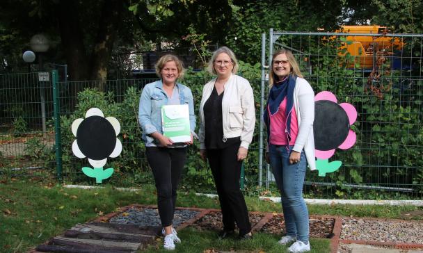 Drei Personen stehen vor einem geschmückten Zaun.