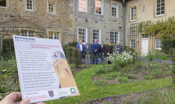 Eine Personengruppe steht in einem Gartenvor einem historischen Gebäude.