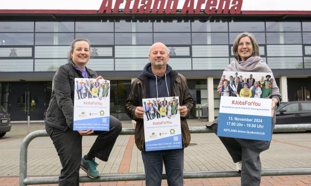Drei Personen stehen vor einem Gebäude mit Glasfassade.