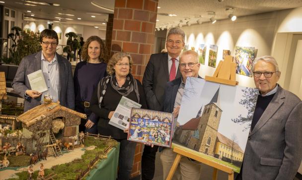 Sechs Personen stehen neben einer Staffelei mit dem Foto einer Kirche.