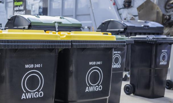 Abfalltonnen mit AWIGO-logo stehen auf einem Hof.
