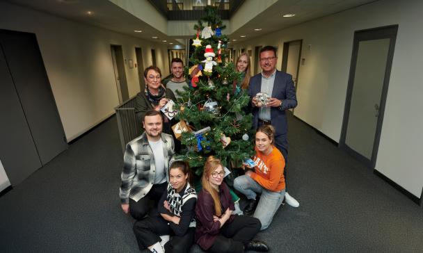 Personengruppe steht um einen Weihnachtsbaum herum.