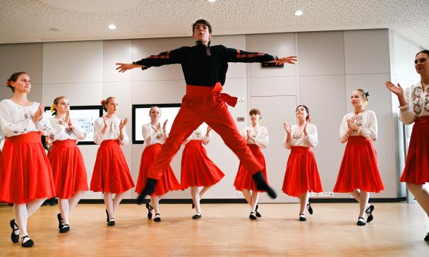 Eine Gruppe tanzendender Personen steht im Halbkreis in einem Foyer.