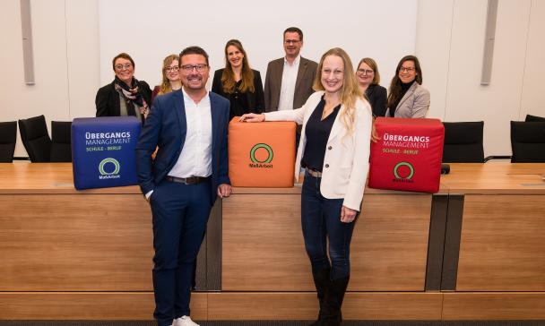 Eine Personengruppe mit bunten Würfeln steht in einem Sitzungssaal.