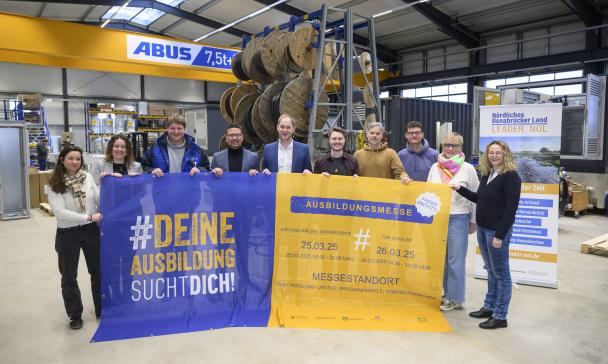 Eine Personengruppe mit einem großen Werbebanner steht in einer Werkshalle.