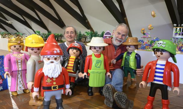 Zwei Personen sitzen zwischen großen Playmobil Spielzeugfiguren.
