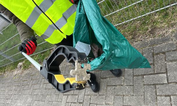 Eine Person mit einer Weste hält eine Abfalltüte und eine Müllzange in den Händen.