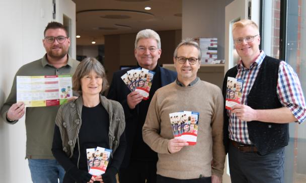 Fünf Personen stehen in einem Flur und halten Flyer in den Händen.