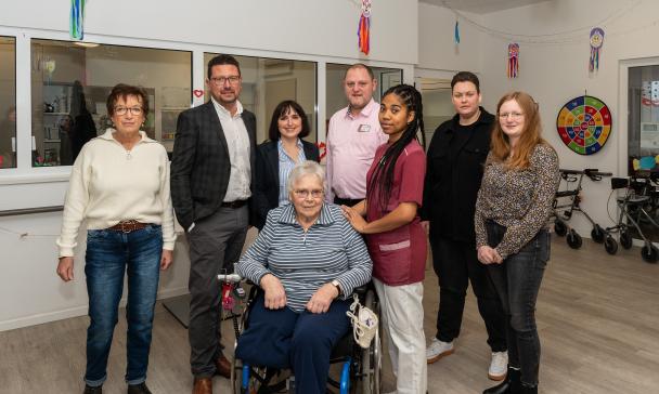 Eine Personengruppe, eine Person sitzt im Rollstuhl, steht in einem Gebäudeflur.