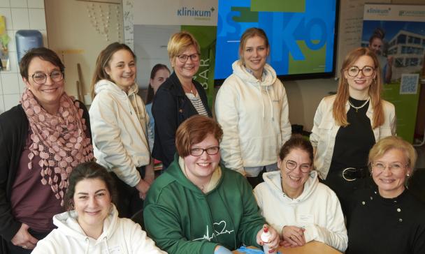 Eine Personengruppe steht und sitzt in einem Klassenzimmer.