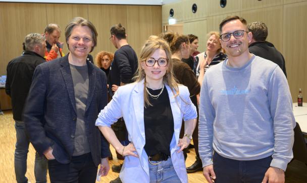 Drei Personen stehen mimt anderen in einem Raum und schauen in die Kamera.