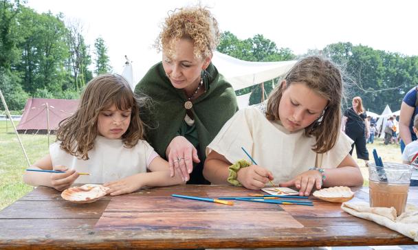Drei Personen in antiken Kostümen sitzen an einem Tisch.