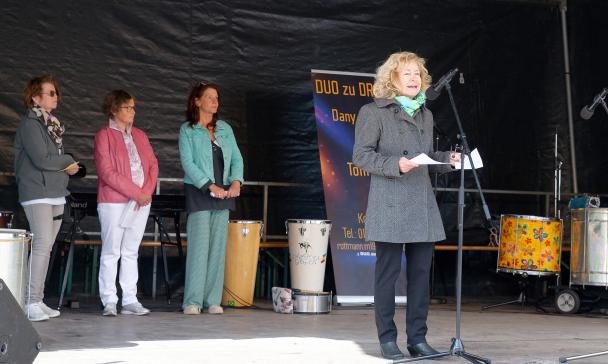 Vier Personen stehen auf einer Bühne, eine davon vorn am Mikrofon.