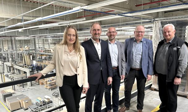 Fünf Personen stehen auf einer Empore in einer Werkhalle.