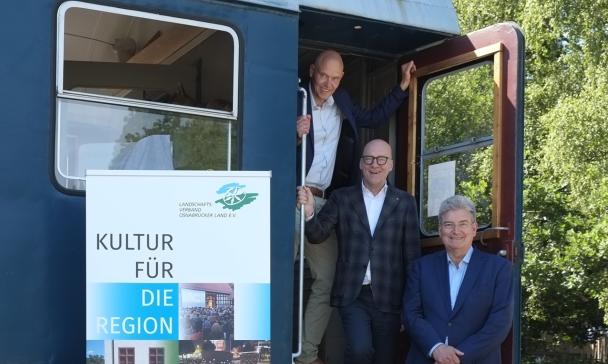 Drei Personen stehen am Einstieg eines Eisenbahnwaggons.