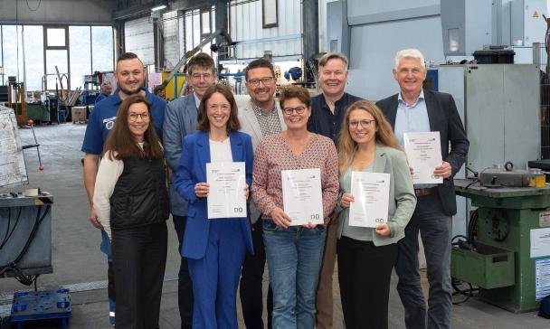 Neun Personen stehen in einer Werkhalle