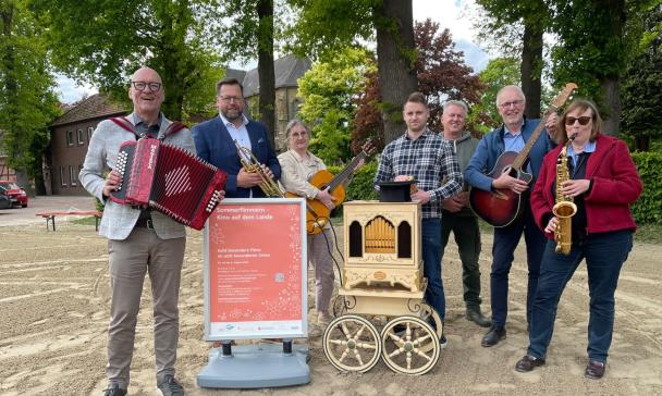 Sieben Personen mit Musikinstrumenten stehen auf einem Hof.
