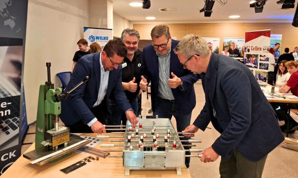 Vier Personen stehen an einem Kickertisch.