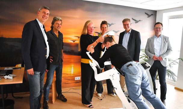 Eine Personengruppe steht in einem Raum vor einem Flugsimulator.