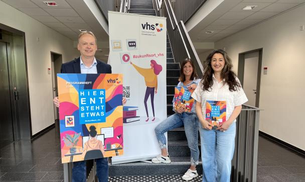 Drei Personen und ein Roll-Up-Poster stehen in einem Flur.