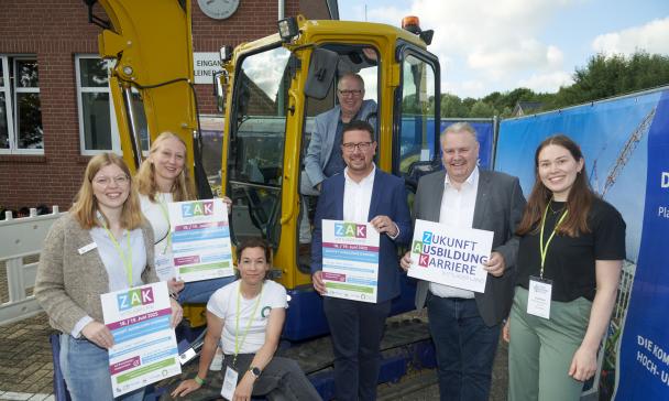 Sieben Personen stehen vor einem Bagger.